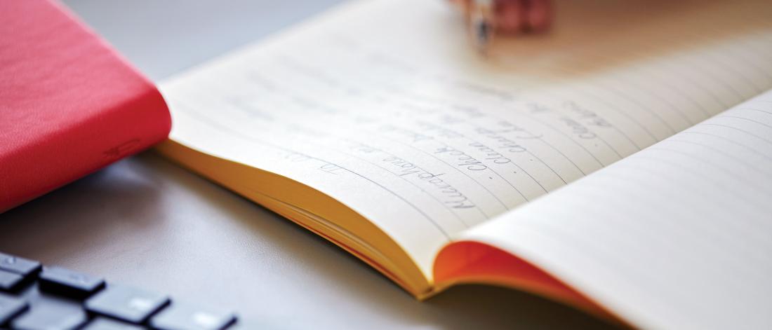 A close up of a student's hand writing notes in a notebook