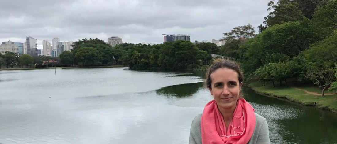 woman looks towards camera with water and cityscape behind