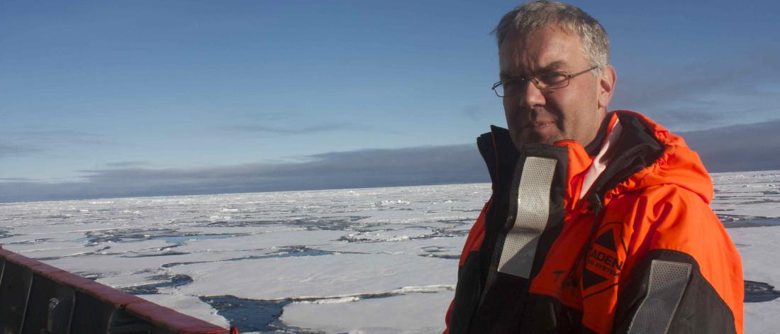 Man on right looks to camera on board a ship, with frozen sea ice in background