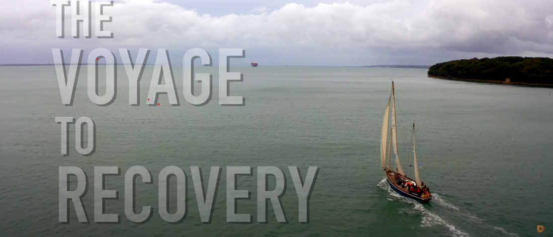 The Voyage to Recovery video screen shot- these words appear to the left of a shot looking down as a sailing boat and some coastline