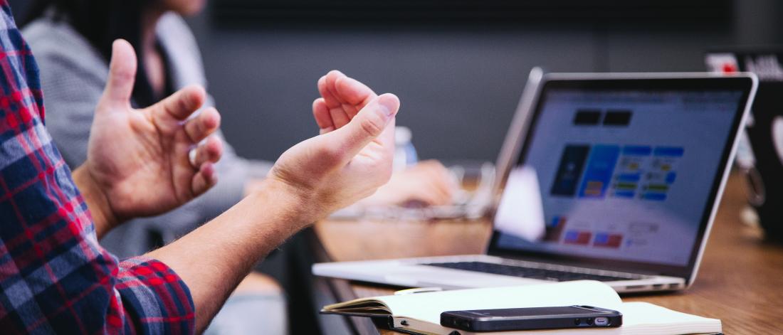  Soeone gesticulates with their hands during an online meeting ( presumably) in front of a laptop computer screen. 