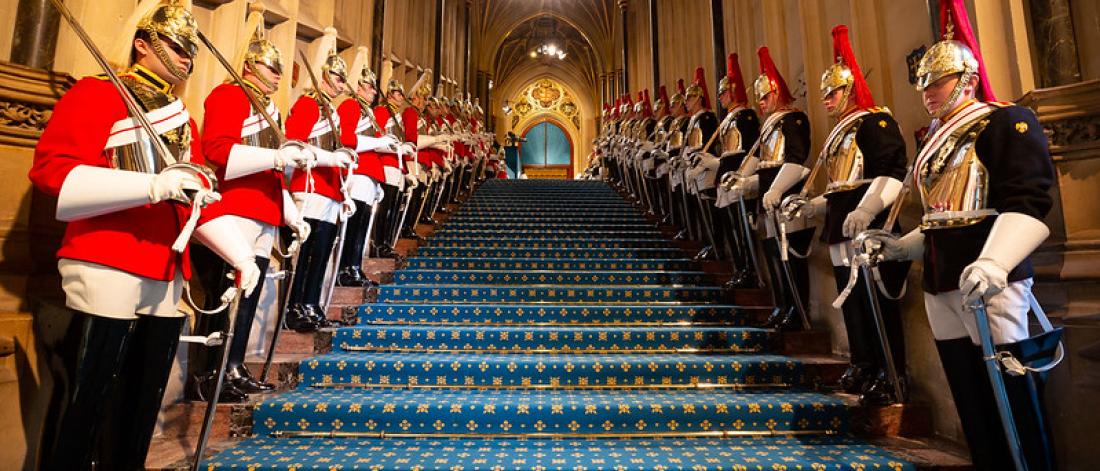 a landscape picture of inside of house of commons on steps are the queens guards all uniformed