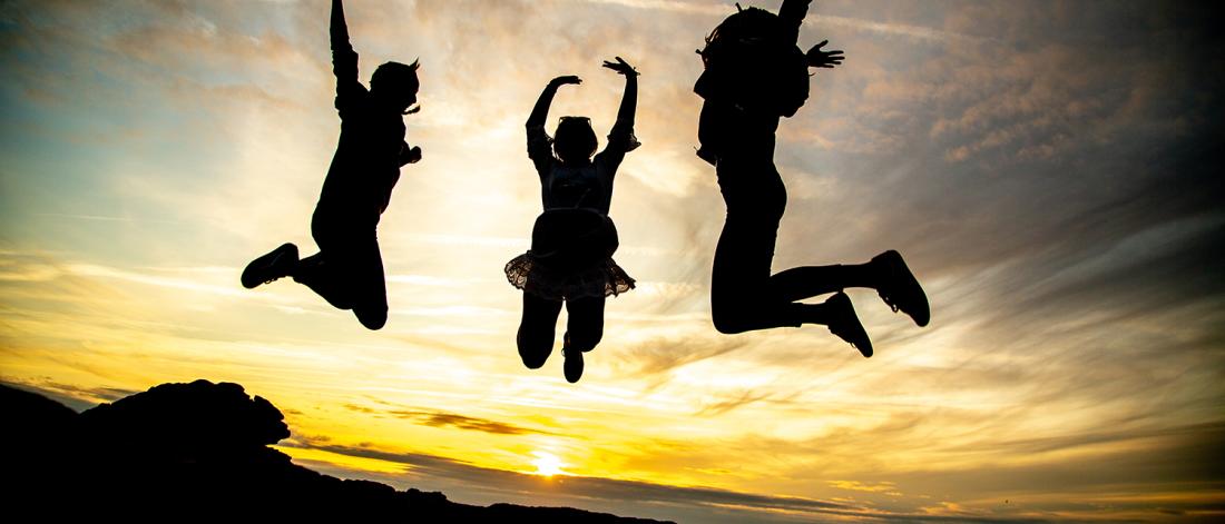 Three people jumping up, with a sunset in the background