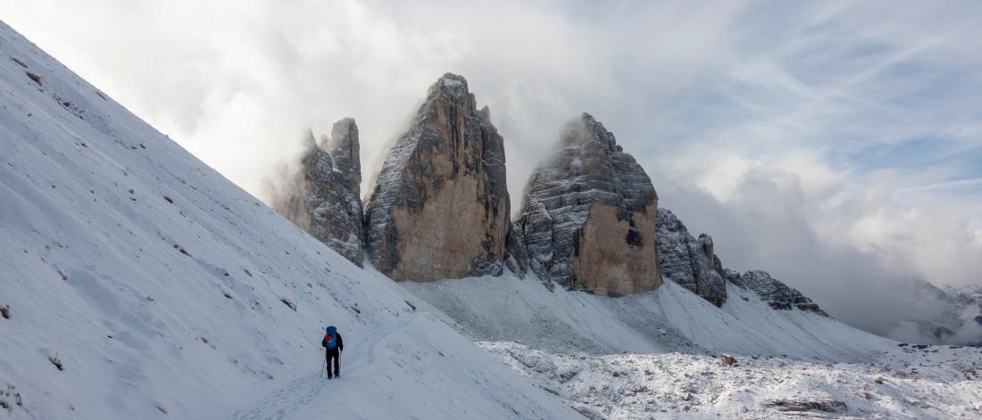 A landscape image of a mountain with three peaks, covered in snow and a person walking towards the summit 