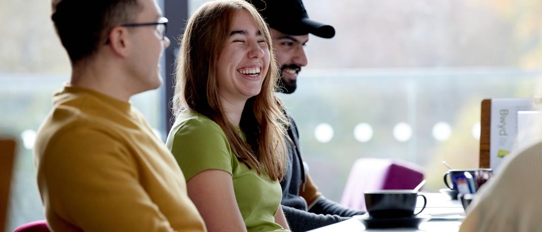 Students sitting at a table in Pontio, laughing and talking over coffee 