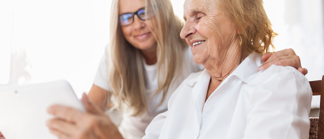 Younger member of family with an elderly member, looking at a tablet screen