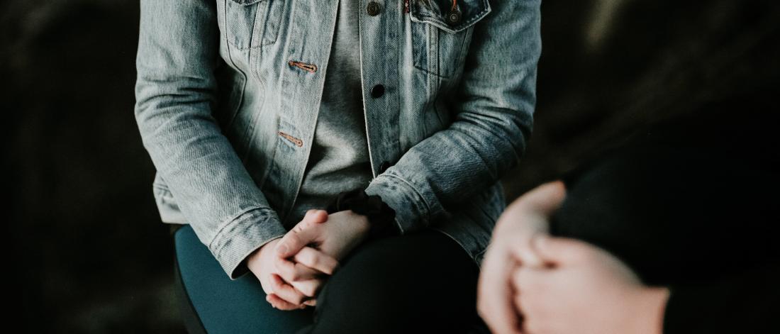 Image of a person sitting down with their hands clasped 