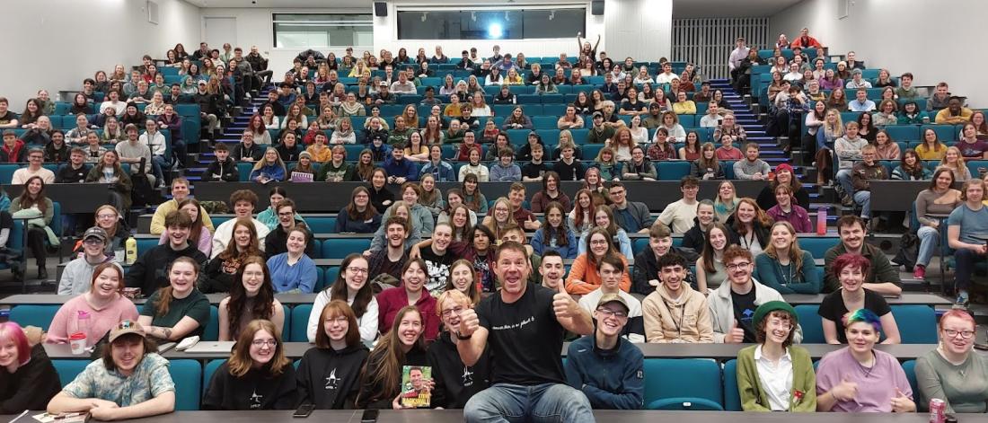 Steve Backshall doing a thumbs up and smiling in front of a lecture theatre full of Bangor University Students