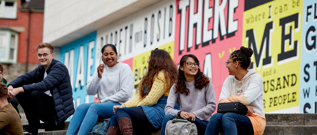 students sitting outside Pontio on the steps in front of a colourful mural.