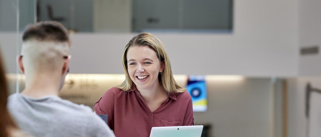 Student studying on laptop whilst talking to another student