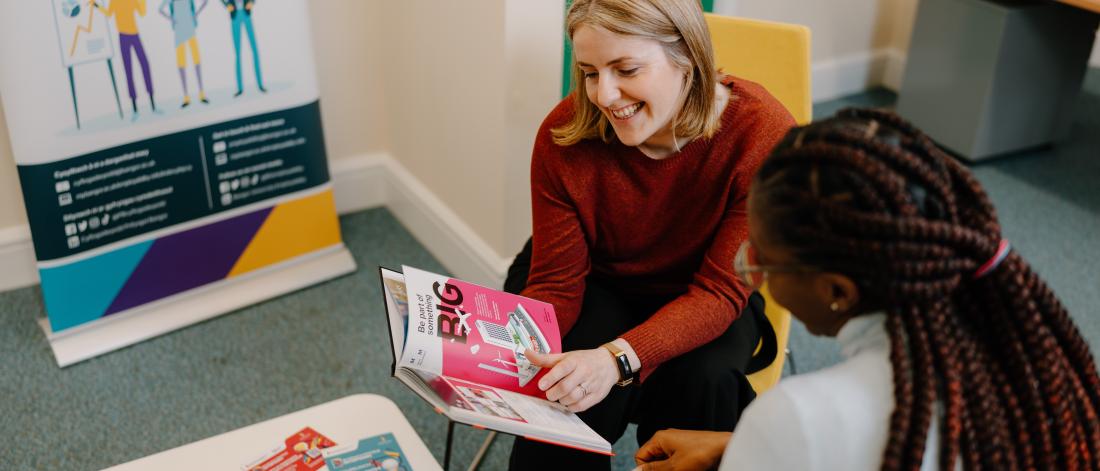 A member of staff speaking to a student and showing them a book about careers and/or employability