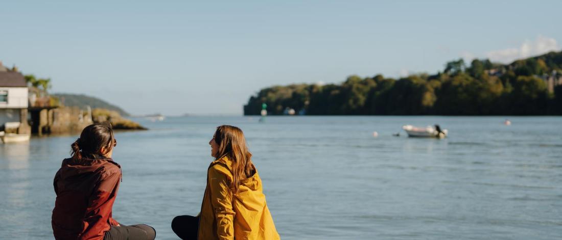 Students sitting on a rock overlooking the Menai Strait