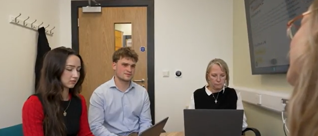 Two students and a lecturer sitting around a table with laptops on the desk chatting to a client in the Legal Advice Clinic.