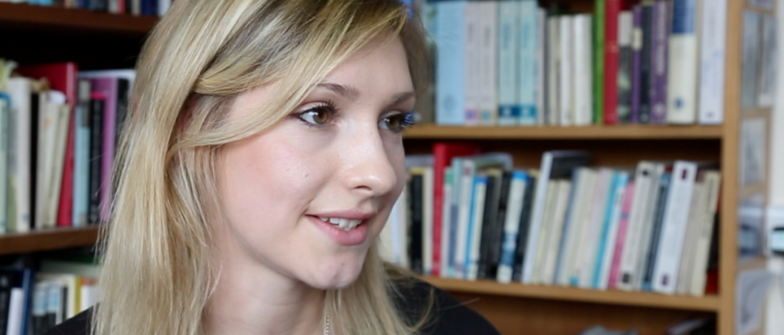 Llun o Carys Roberts yn cael cyfweliad gyda llyfrau yn y cefndir