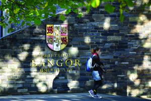 Student walking past the University crest on the wall at main arts