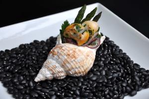 a cooked whelk on a bed of black beans on a square white plate
