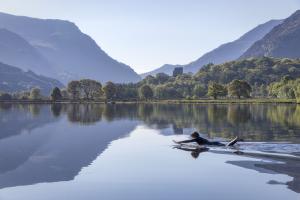 a paddleboarder lies on a paddleboard on Llyn Padarn Padarn Lake with  Snowdonia and the Llanberis Pass as a backdrop
