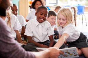 Primary aged children sit on the floor around a book