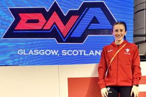 Llun o Ffion Roberts - athletwraig o flaen banner glas gyda'r geiriau DNA Glasgow Scotland