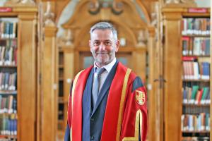 Besuited man stands in red academic gown in Library