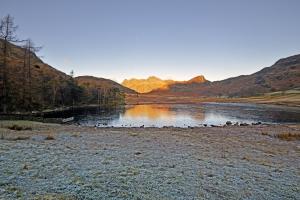 A frozen lake with sunlight on a far mountain