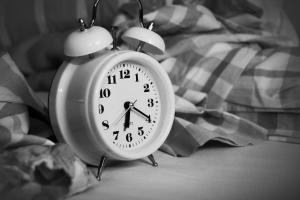  a black and white image of an old fashioned type of alarm clock next to a bed, the time is 6.20