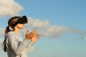 Woman wearing virtual reality headset with blue sky and white clouds in the background