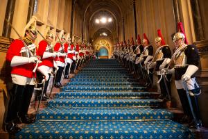 a landscape picture of inside of house of commons on steps are the queens guards all uniformed