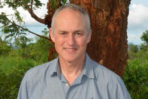 person smiling with short sleeved shirt in front of a tree