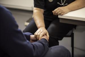 A close up of a doctor (stethoscope seen hanging from neck), places hand over patient's clasped hands.