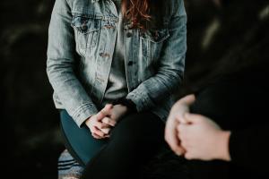 Image of a person sitting down with their hands clasped 