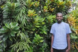 Llun Abdoulkader Fardane, aelod o staff Dahari, yn sefyll o flaen gwyrddni