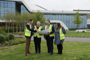  four people in hi viz look at plans outside the current building.