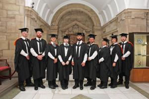 Six individuals in graduation gowns with certificates