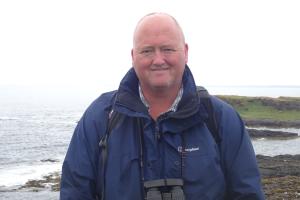 Dr Mark Mainwaring on the coast with binoculars around his neck