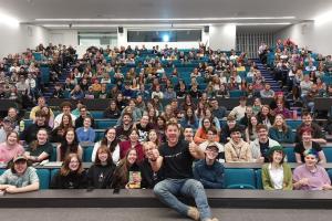 Steve Backshall yn chwifio'i fodiau o flaen darlithfa lawn