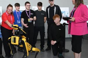 A group of students and an operator looking at a Dog-like robot that is black and yellow