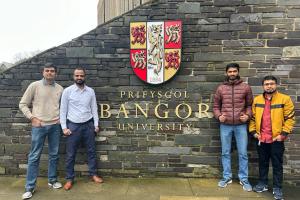 Four students standing in front of a wall with the Bangor University crest 