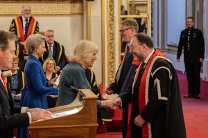 Is-Ganghellor ac Athro Bangor yn derbyn medal a sgrôl gan y Teulu Brenhinol ym Mhalas Buckingham