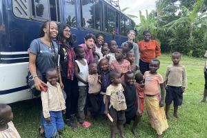 Students on the Mount Elgon fieldwork trip in Uganda standing with local children next to a bus  