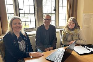 Three people sat at a desk looking at the camera