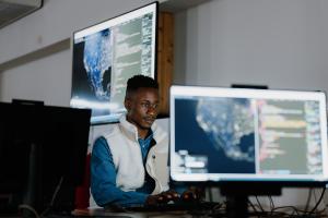 A student sitting in front of a computer with a large screen in the background and a smaller screen in the foreground  