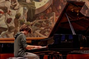 Student pianist performing in concert in front of a fine art painting