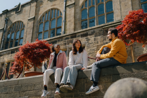 Three young people chatting outside a big old building