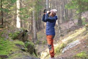 woman standing in forest looks through binoculars