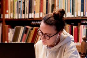 Student sitting in the library with a laptop and books on shelves in the background