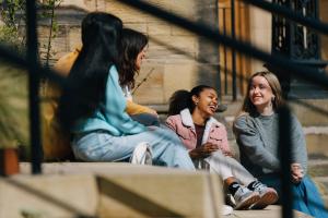 Grŵp o fyfyrwyr yn eistedd ar stepiau yn sgwrsio 