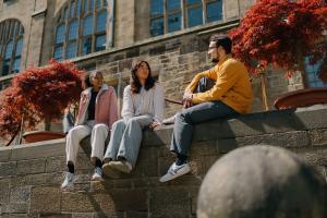 Grŵp o fyfyrwyr yn eistedd ar y wal yn y cwad mewnol yn sgwrsio 