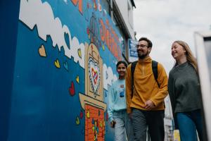 Three students walking in Bangor High Street next to wall mural