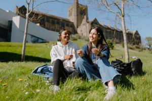 A photo of two students sitting on the grass talking to each other outside of Pontio.